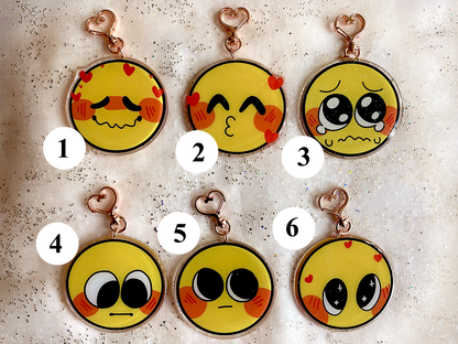 Six acrylic charms, numbered one through six. Charm 1 is an emoji making a lovey face. Charm 2 is an emoji making a kissing face. Charm 3 is a crying emoji. Charm 4 is an emoji blushing and looking down. Charm 5 is an emoji blushing and looking up. Charm 6 is an emoji with sparkles in its eyes.