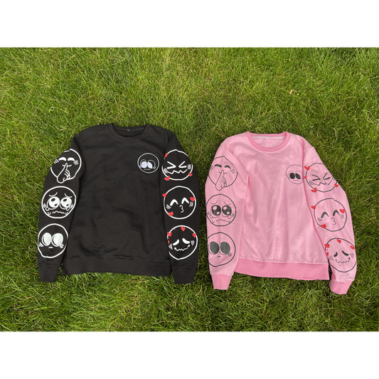 Two nice emoji sweaters side by side. The sweater on the left is black, and the sweater on the right is pink. Both feature various emoji designs on the front and sleeves.