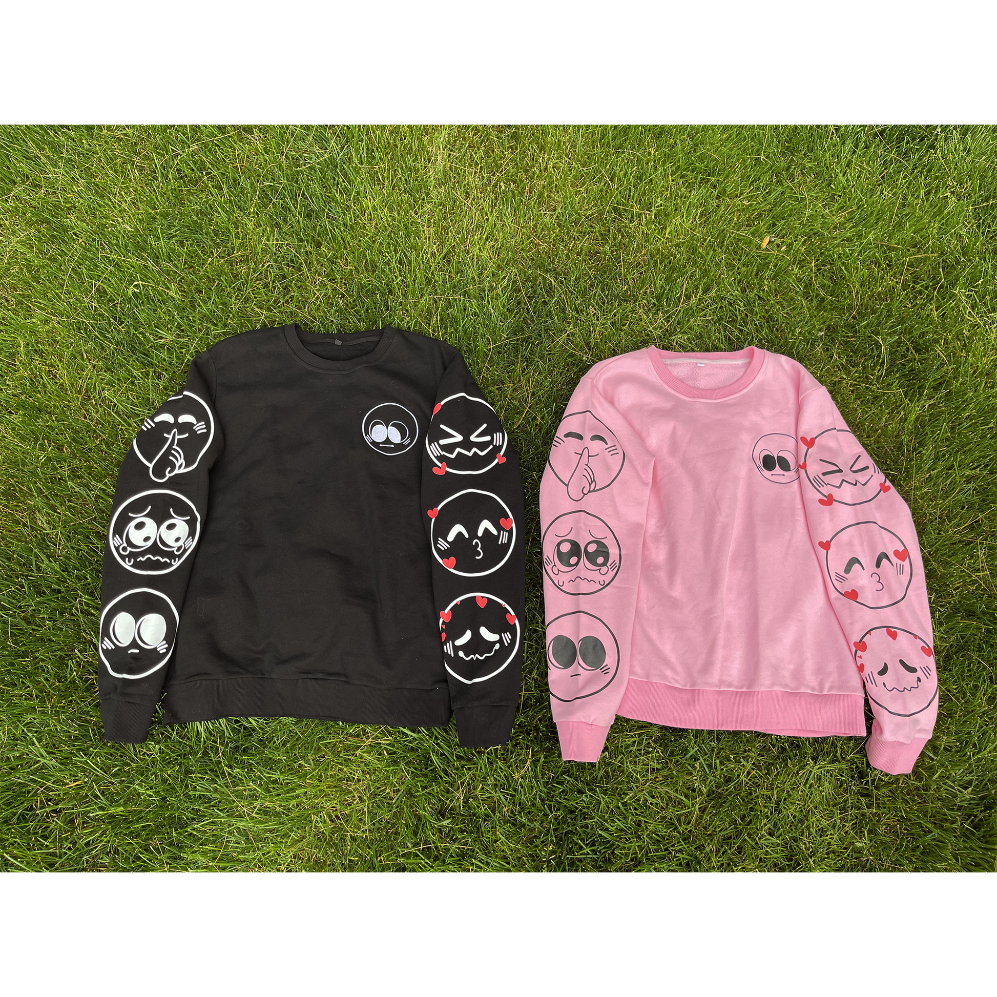 Two nice emoji sweaters side by side. The sweater on the left is black, and the sweater on the right is pink. Both feature various emoji designs on the front and sleeves.